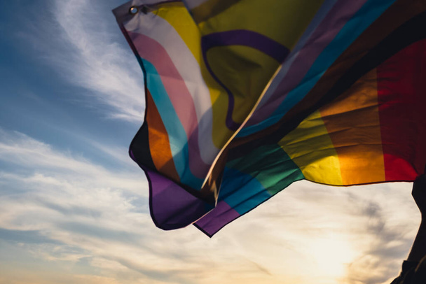 Ταυτότητα φύλου. Defocused Rainbow LGBTQIA σημαία κυματίζει στον άνεμο κατασκευασμένο από μετάξι υλικό σε φόντο τομέα. Σύμβολο του μήνα υπερηφάνειας ΛΟΑΤΚΙ. Ίσα δικαιώματα. Έννοια ειρήνης και ελευθερίας - Φωτογραφία, εικόνα