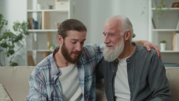 Young and elderly men share life experiences, sitting on a couch, discussing personal stories, psychological support, cross-generational understanding, heart-to-heart talks, family communication - Footage, Video