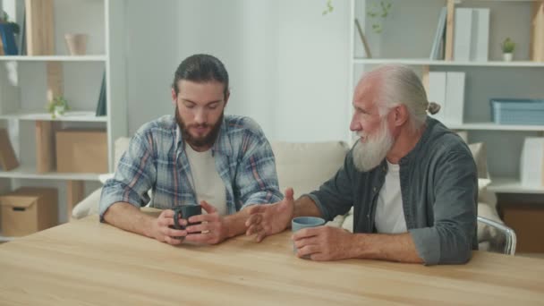 Dwoje przyjaciół, młody mężczyzna i starszy mężczyzna, siedzą przy stole, omawiając sytuacje życiowe i zapewniając sobie wsparcie psychologiczne, przyjazną komunikację, dialog międzypokoleniowy. - Materiał filmowy, wideo