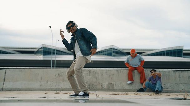 Handsome break dancer enjoy perform freestyle movement with asian friend cheering behind. Hipster listen to music from headphone and looking at camera. Street dance. Outdoor sport 2024. Sprightly. - Photo, Image