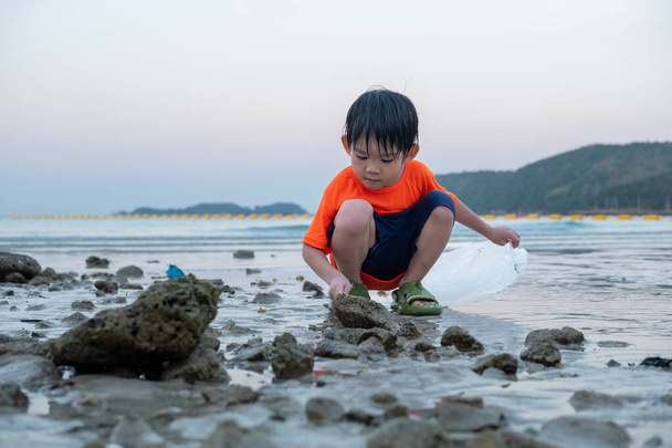 Petit garçon asiatique aide ramasser les ordures sur la plage de la mer. - Photo, image