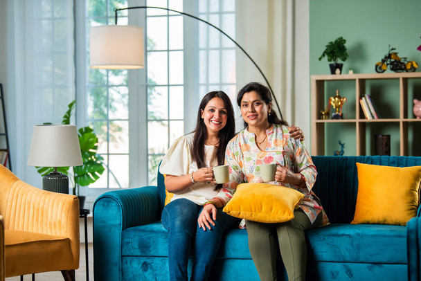 Зріла індійська мати з дорослим дочка розслабляється на дивані має каву вдома - Фото, зображення