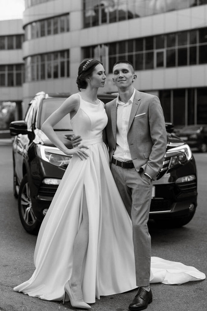 mariée et marié avec une voiture noire près d'un gratte-ciel en verre - Photo, image