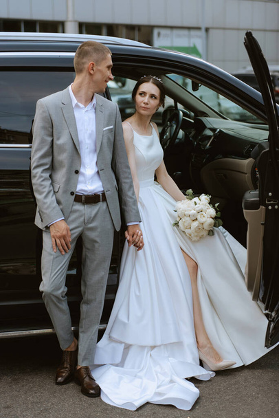 bruid en bruidegom met een zwarte auto bij een glazen wolkenkrabber - Foto, afbeelding