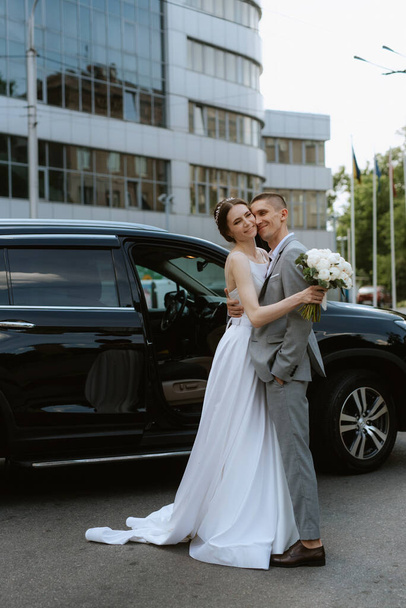 menyasszony és vőlegény egy fekete autó mellett egy üveg felhőkarcoló - Fotó, kép