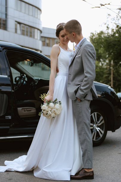 nevěsta a ženich s černým autem v blízkosti skleněného mrakodrapu - Fotografie, Obrázek