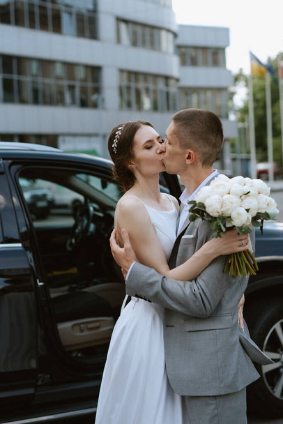 sposa e sposo con una macchina nera vicino a un grattacielo di vetro - Foto, immagini
