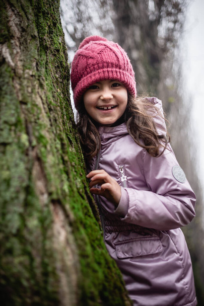 portret uśmiechniętej dziewczyny ukrywającej się za drzewem w różowym kapeluszu - Zdjęcie, obraz