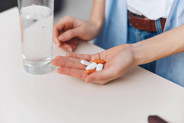 Женщина, держащая бутылку таблеток рядом со стаканом воды на столе в образе концепции здравоохранения - Фото, изображение