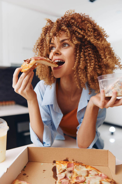 gekrulde vrouw genieten van een heerlijke plak pizza in de voorkant van een verleidelijke doos van pizza - Foto, afbeelding