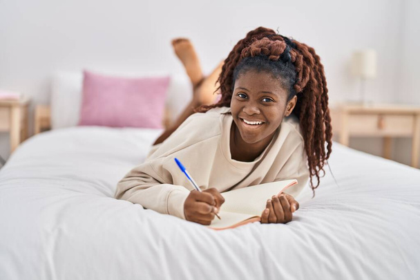 Afro-Amerikalı kadın, yatak odasında, deftere yazı yazıyor. - Fotoğraf, Görsel