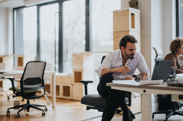 Un empresario profesional se centra intensamente en su portátil en un espacio de oficina contemporáneo bien iluminado, lo que sugiere productividad y dedicación. - Foto, imagen