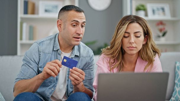 Мужчина и женщина делают покупки с ноутбуком и кредитной картой, сидя дома на диване - Фото, изображение