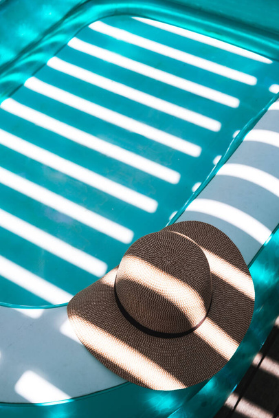 a stylish summer hat laid gracefully by the side of a refreshing turquoise paddling pool on a bright, sun-drenched day - Photo, Image
