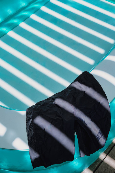 pár barevných plaveckých trenýrek položených po straně osvěžujícího tyrkysového brouzdaliště za jasného slunečného dne - Fotografie, Obrázek