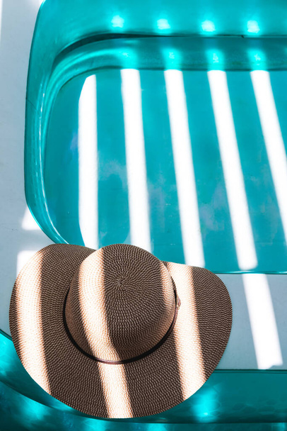 Güneşli, güneşli bir günde ferahlatıcı bir turkuaz yüzme havuzunun kenarına serilmiş şık bir yaz şapkası. - Fotoğraf, Görsel