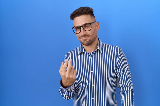 Homme hispanique avec barbe portant des lunettes signe venir ici geste avec la main invitant accueillant heureux et souriant  - Photo, image