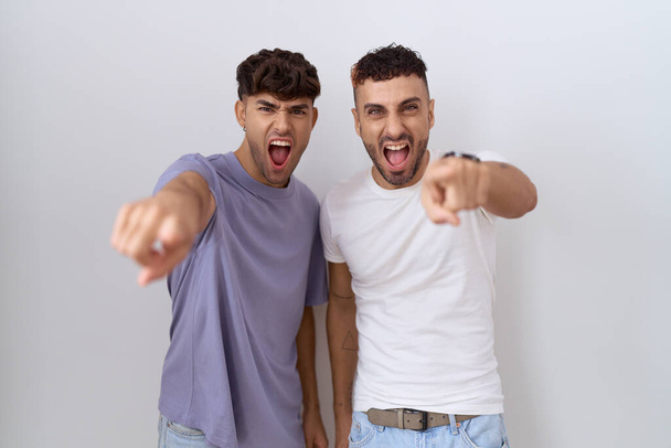 couple gay homosexuel debout sur fond blanc pointant mécontent et frustré à la caméra, en colère et furieux contre vous  - Photo, image