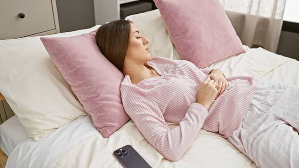Жінка спокійно спить на ліжку в сучасній спальні, її смартфон відпочиває поруч. - Фото, зображення