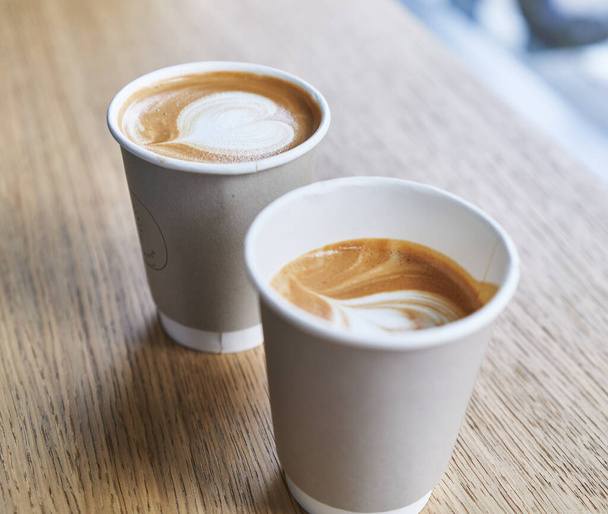 Dwa kubki cappuccino na wynos z latte w kształcie serca, siedzące na drewnianym stole.. - Zdjęcie, obraz