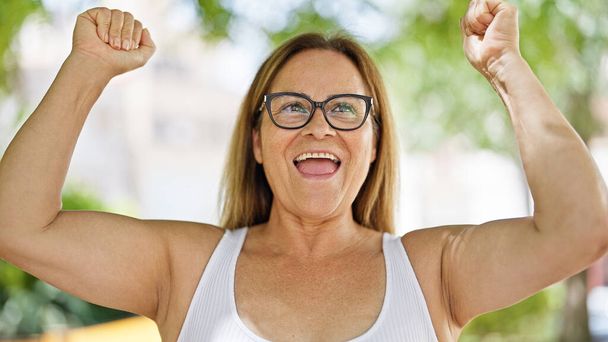 Mujer hispana de mediana edad con gafas celebrando en el parque - Foto, imagen