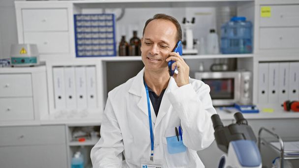 Hombre científico de mediana edad hablando en smartphone sonriendo en el laboratorio - Foto, imagen
