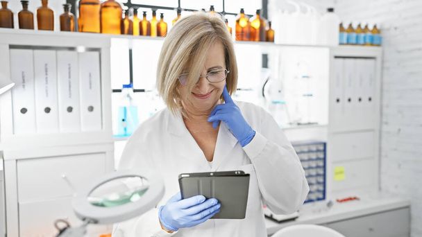 Hymyilevä nainen tiedemies tabletin kanssa laboratoriossa, pullojen ja laitteiden ympäröimänä. - Valokuva, kuva
