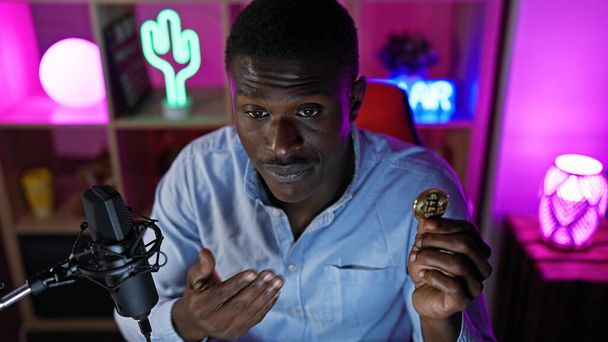 Homme africain tenant Bitcoin avec microphone dans une salle de jeux colorée et éclairée la nuit - Photo, image
