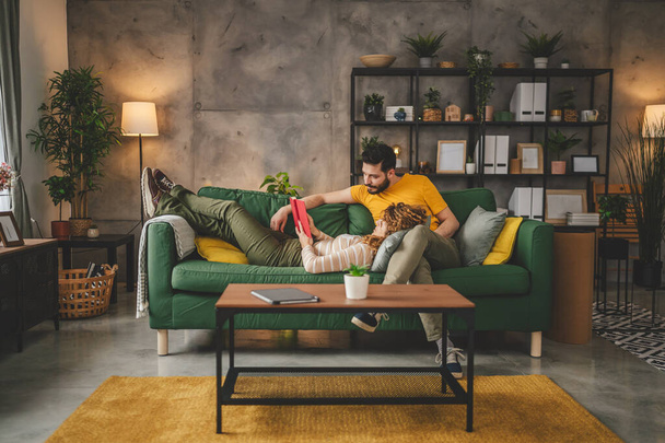 男と女性の慎重な大人のカップルはソファーベッドの自宅で本を読む - 写真・画像