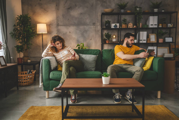 homem e mulher branco casal adulto ler livro e usar tablet digital em casa no sofá-cama separado - Foto, Imagem