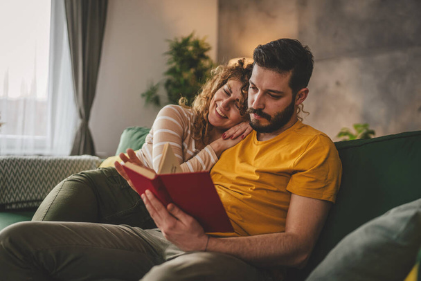 男と女性の慎重な大人のカップルはソファーベッドの自宅で本を読む - 写真・画像
