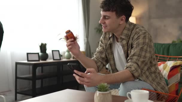 Yksi mies pitää lääke huumeiden pullo pillereitä lue etiketti matkapuhelimeen - Materiaali, video