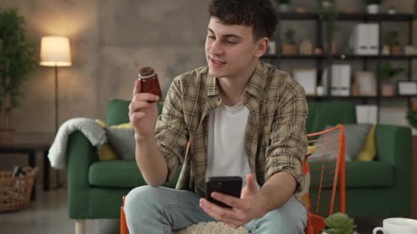 Egy férfi gyógyszeres üveg tablettákat tart olvasás címke mobiltelefon - Felvétel, videó