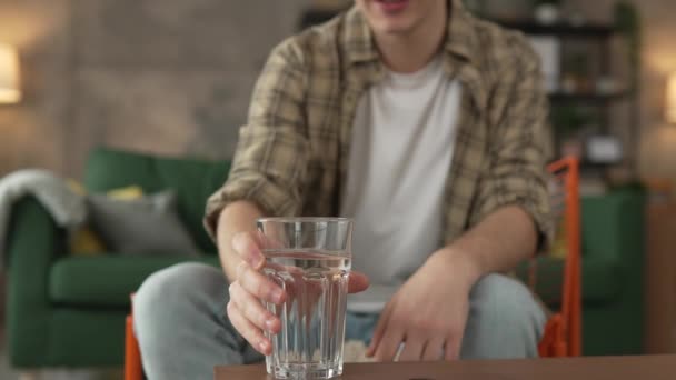retrato de hombre joven caucásico adolescente celebrar vaso de agua en casa - Imágenes, Vídeo