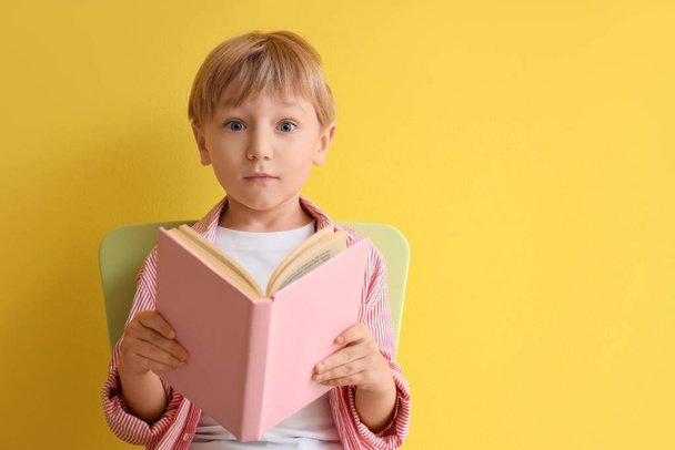 Menino surpreso com livro sentado na cadeira contra fundo amarelo - Foto, Imagem