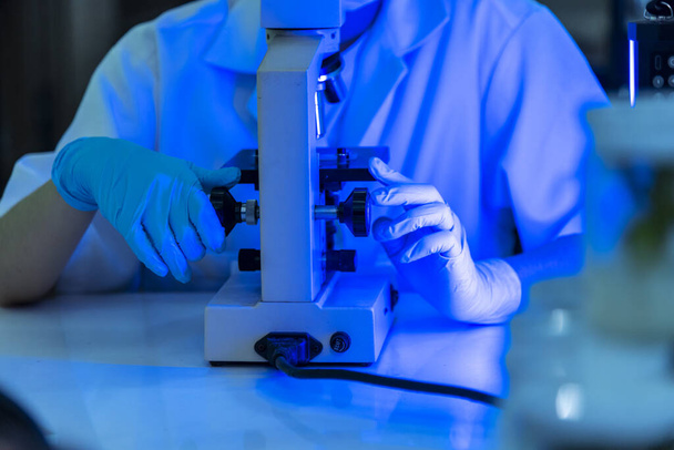 Vrouwelijke technicus laboratorium te analyseren genetisch onderzoek. Vrouw wetenschapper in het lab kijken naar de wetenschap microscoop medische test onderzoeken biologie chemie in blauw licht zwarte achtergrond. Chemie Medische - Foto, afbeelding