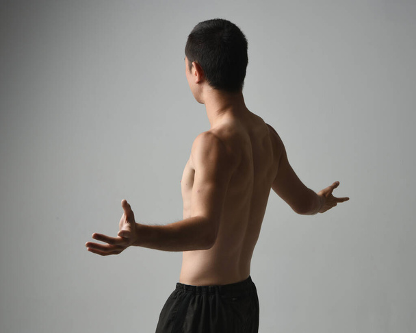 Κοντινό πορτραίτο ενός ταιριαστού Ασιάτη αρσενικού μοντέλου, χωρίς μπλούζα και μύες. gestural ti chi εμπνευσμένο ποζάρουν με τα χέρια απλώνονται. Απομονωμένο σε λευκό φόντο στούντιο με κυκλοθυμική σιλουέτα. - Φωτογραφία, εικόνα