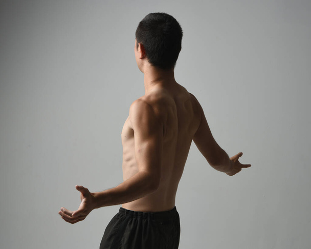 Κοντινό πορτραίτο ενός ταιριαστού Ασιάτη αρσενικού μοντέλου, χωρίς μπλούζα και μύες. gestural ti chi εμπνευσμένο ποζάρουν με τα χέρια απλώνονται. Απομονωμένο σε λευκό φόντο στούντιο με κυκλοθυμική σιλουέτα. - Φωτογραφία, εικόνα