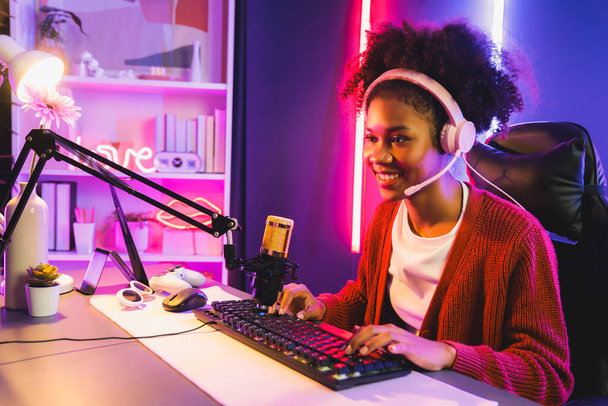 Africká americká dívka streamer hrát online boj s Esport zkušený tým nosí sluchátka v neonové barvě osvětlovací místnosti. Mluvit s ostatními hráči plánování strategie vyhrát konkurenty. Tastemaker. - Fotografie, Obrázek