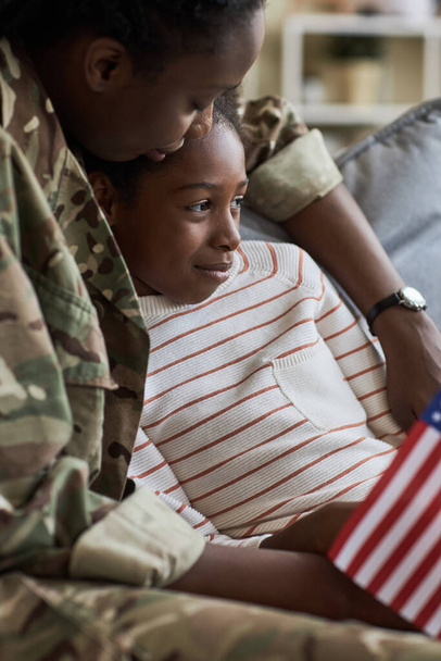 Image verticale de maman rentrant du service de guerre, assise sur le canapé avec sa fille et l'embrassant - Photo, image