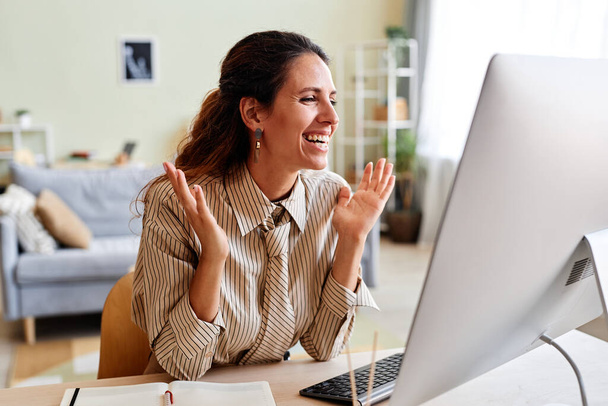 Portrait franc de joyeuse femme adulte en appel vidéo riant émotionnellement sur le lieu de travail - Photo, image