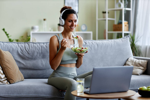 Портрет спортивної молодої жінки, що їсть свіжий салат, насолоджуючись здоровим способом життя та органічним харчуванням вдома - Фото, зображення
