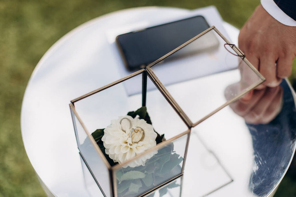 Accesorios de ceremonia de boda. Anillos de boda en una elegante caja de vidrio moderna en una flor - Foto, imagen
