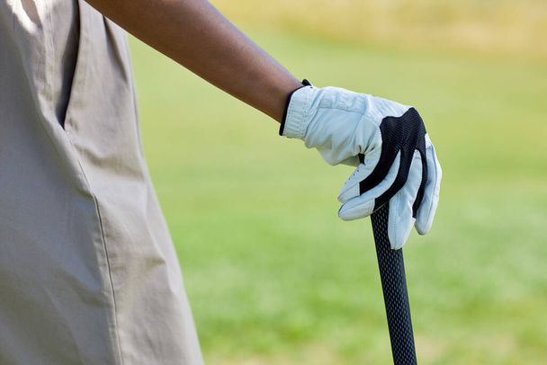 Primer plano de la mano femenina con guantes que sostiene el club de golf al aire libre contra el campo verde, espacio de copia - Foto, imagen