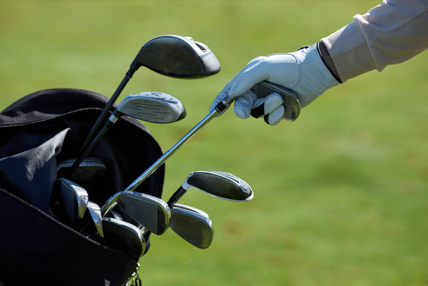 Крупный план неузнаваемого игрока в гольф, выбирающего клуб и вынимающего из сумки для гольфа на зеленом фоне - Фото, изображение