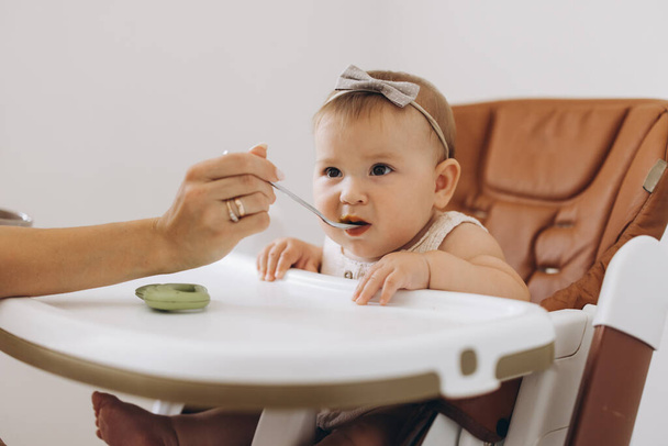 Mother feeding healthy food to her adorable little daughter sitting in high chair - Photo, Image