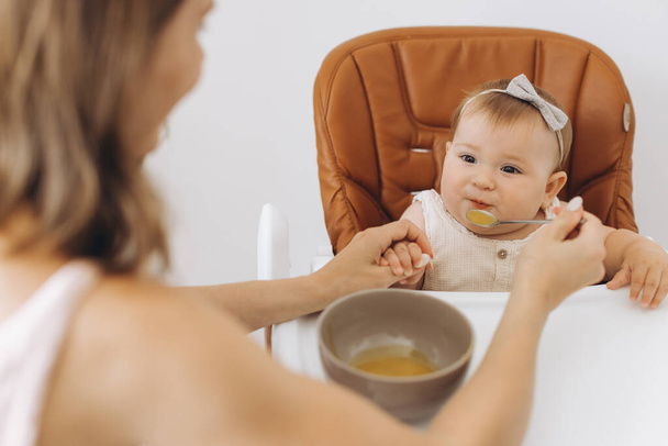 ハイチェアに座っている彼女の愛らしい小さな娘に健康的な食べ物を与える母 - 写真・画像