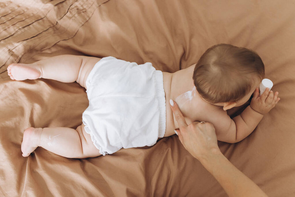 Feliz madre aplicando crema en el cuerpo de su bebé - Foto, imagen