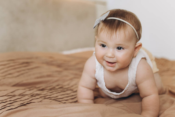 Portré egy kislányról, aki mosolyog és mászik az ágyon a hálószobában. - Fotó, kép