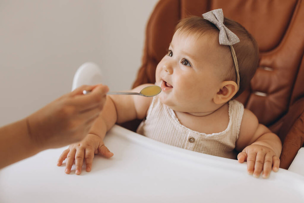Mãe alimentando comida saudável para sua adorável filhinha sentada em cadeira alta - Foto, Imagem